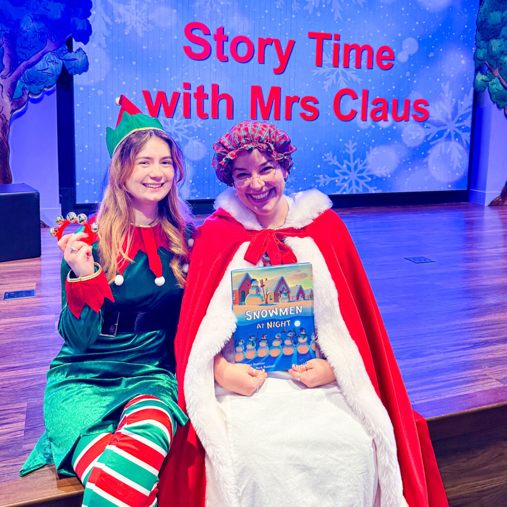 Mrs. Claus and elf with book and bells on stage of Story Time Theater